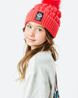 Young girl wearing a red beanie with a pom-pom on a white background