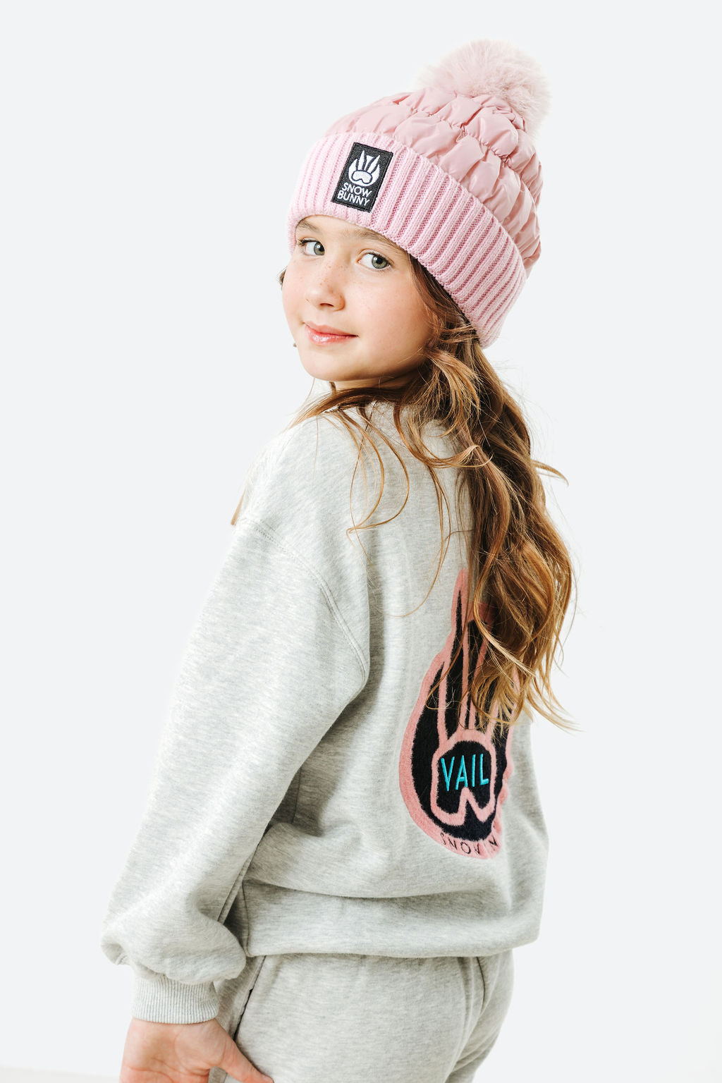 Child wearing a pink beanie and gray sweatshirt with a logo on a white background