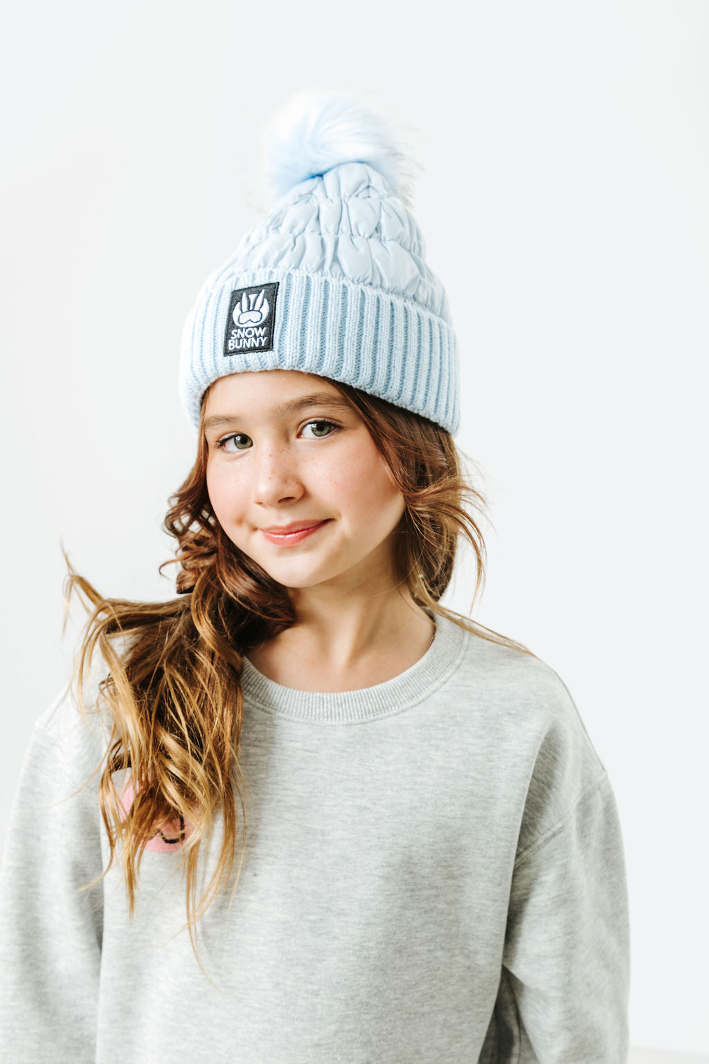 Person wearing a light blue beanie with a logo on a white background