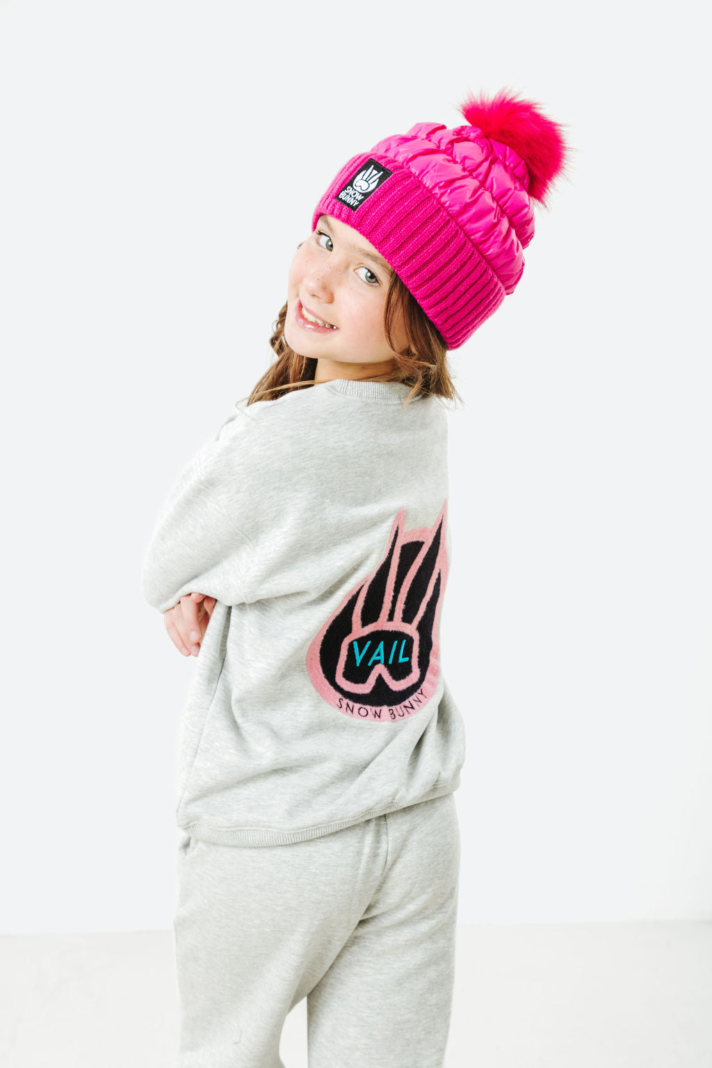 Child wearing a pink beanie and gray sweatshirt with a logo on a white background