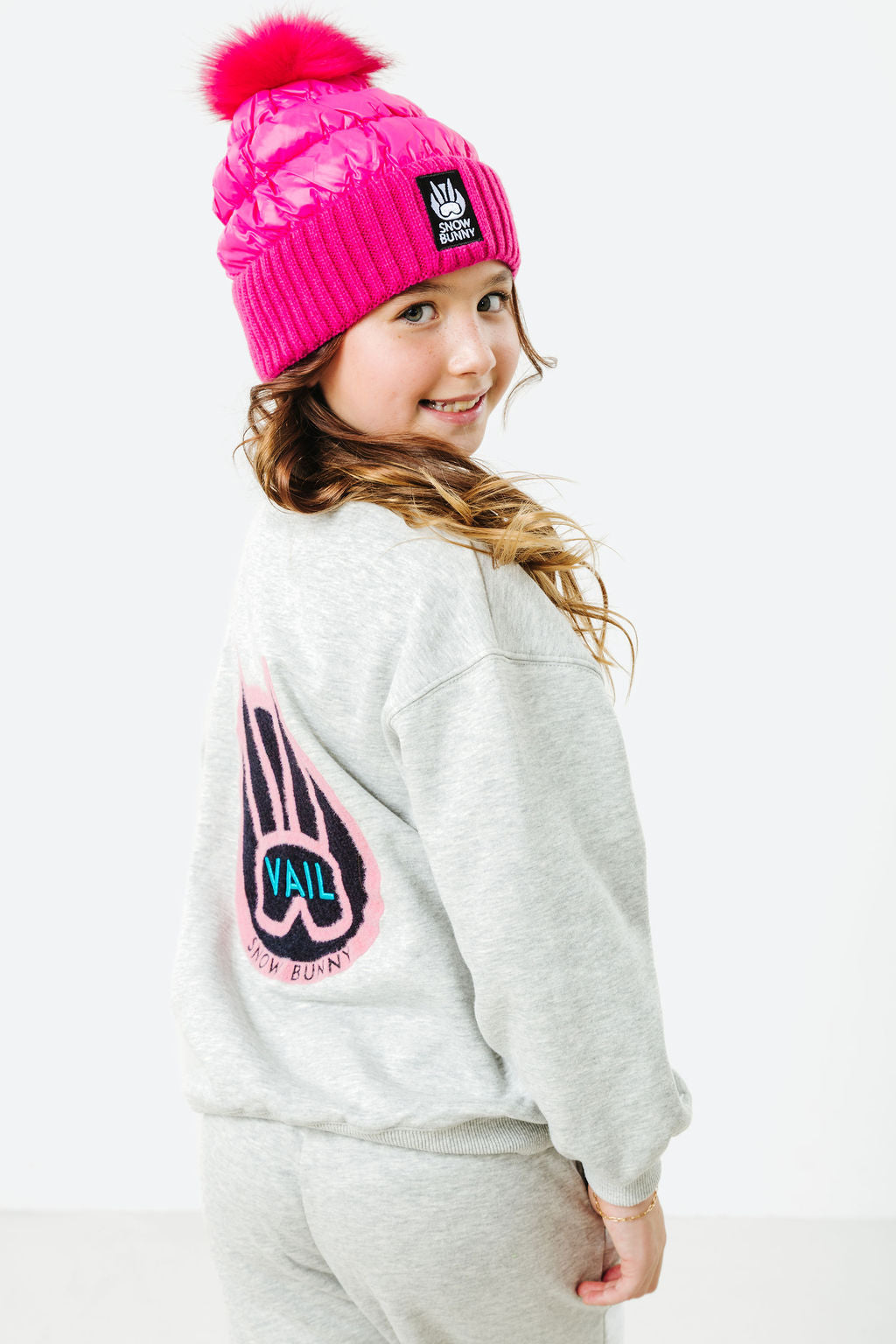 Child wearing a pink beanie and gray sweatshirt with a logo on a white background