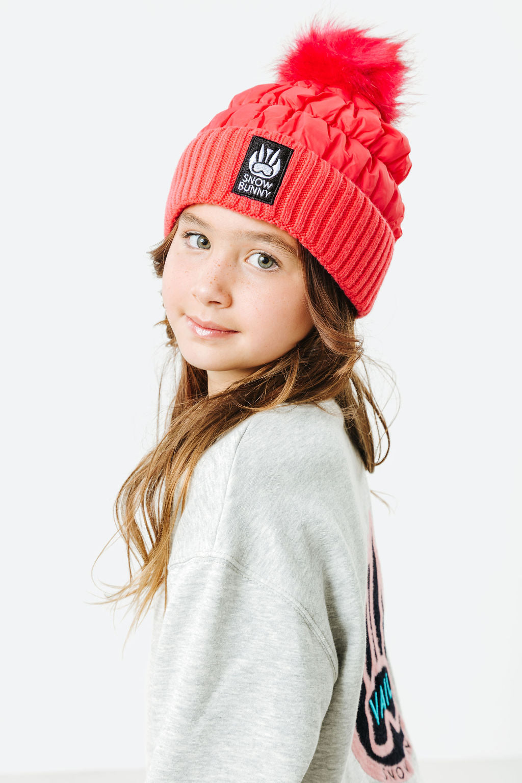 Young girl wearing a red beanie with a pom-pom on a white background