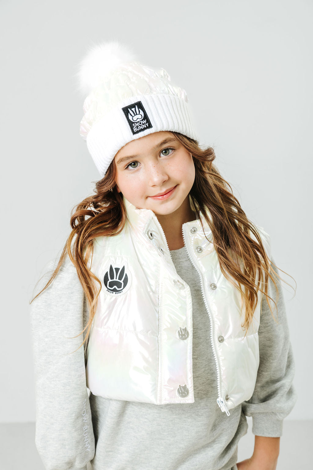 Child wearing a white beanie and jacket with logos on a light gray background