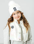 Child wearing a white beanie and jacket with logos on a light gray background