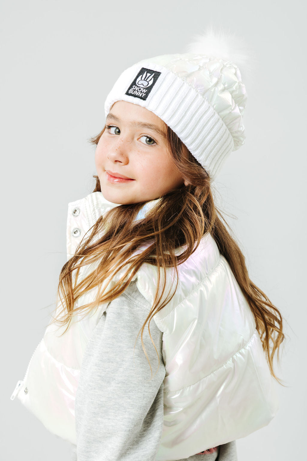 Young girl wearing a white beanie and puffer jacket on a light gray background