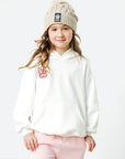 Young girl wearing a white hoodie and pink pants with a beige knit hat on a white background
