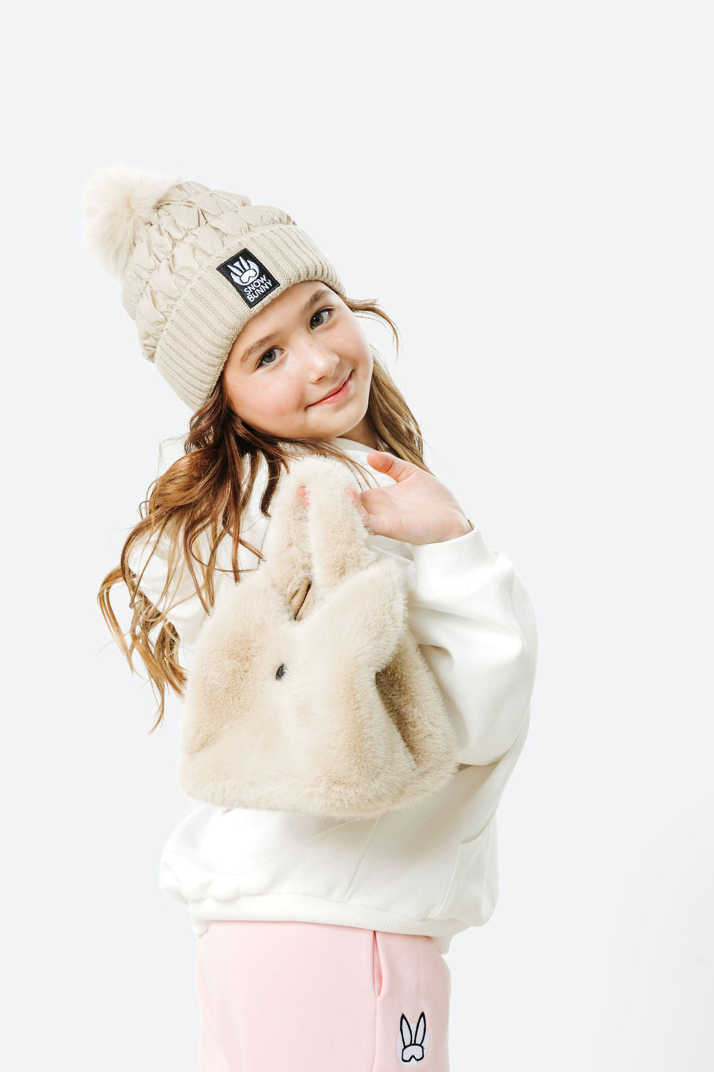 Child wearing a cream beanie, sweater, and pants with a white background