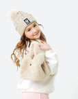 Child wearing a cream beanie, sweater, and pants with a white background