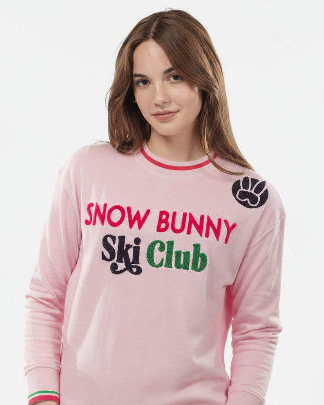 Person wearing a pink 'Snow Bunny Ski Club' outfit on a white background